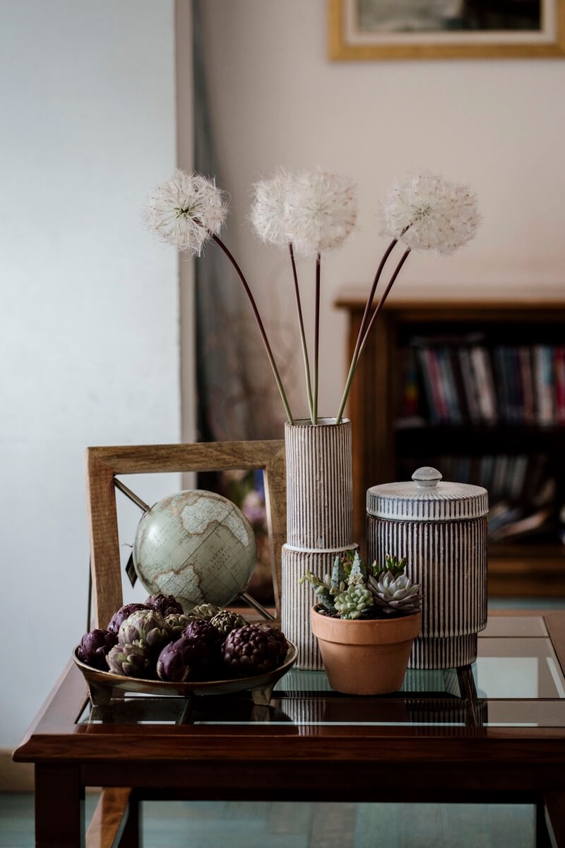 Sun un tavolinetto da salotto: vaso e cilindro a righe in ceramica, mappamondo anticato con cornice di legno, piantina succulenta in vaso e carciofi